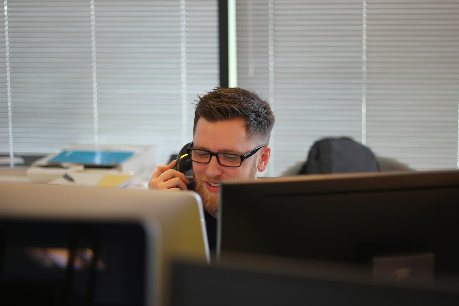 A sales rep on a call, seen across the office over a row of monitors